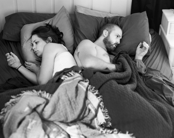 Couple in bed facing away from each other clutching empty space - mobile phone's photoshopped out